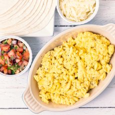Scrambled eggs in a dish with tortillas, salsa and grated cheese on the side.