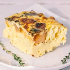 Square slice of frittata with potatoes, onions and cheddar on a white plate, garnished with herbs.