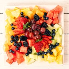Pieces of seasonally ripe fruit (melons, pineapplem berries and grapes) on a platter.