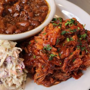 Tender pulled BBQ chicken glistening with tangy-sweet sauce, served alongside molasses baked beans and creamy coleslaw