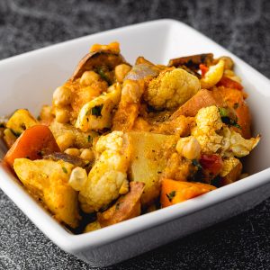Colorful vegetable tagine featuring chickpeas, roasted cauliflower, sweet potatoes, and carrots in a white square bowl